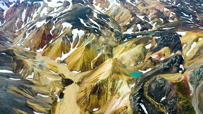 Aerial view of a snowed mountain range and colored mountains in the highlands of Landmannalaugar, Iceland.