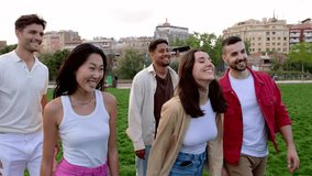 Confident group of young friends having fun walking together outdoors. Millennial teenage people enjoying time at city park. Friendship and community concept. Slow motion video.