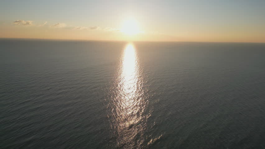 High angle drone shot of the sun over the ocean horizon.
