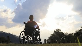 Person sitting on a wheelchair enjoying with raised hands on the mountain at the sunset time. - Powered by Shutterstock - Get 15% off with code: PIKWIZARD15
