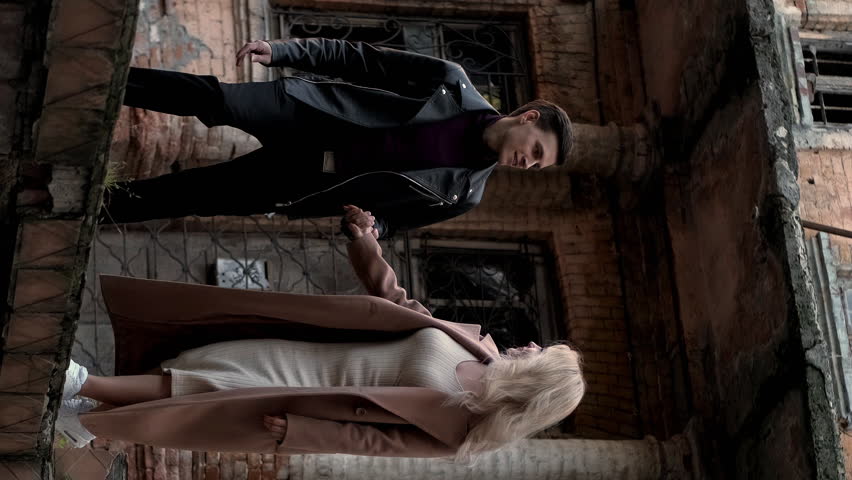 Vertical video. Old city walk. Urban date. Romantic weekend. Carefree happy couple in love holding hands enjoying strolling together outside on street with abandoned house.