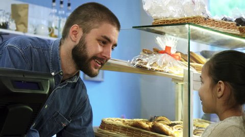 Attractive male baker talking to a little girl at his bakery store