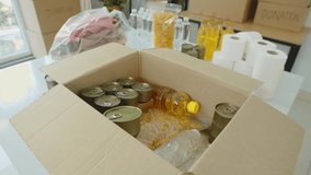 Handheld shot of canned goods, cooking oil, macaroni and other food in donation box on table in volunteer center - Powered by Shutterstock - Get 15% off with code: PIKWIZARD15