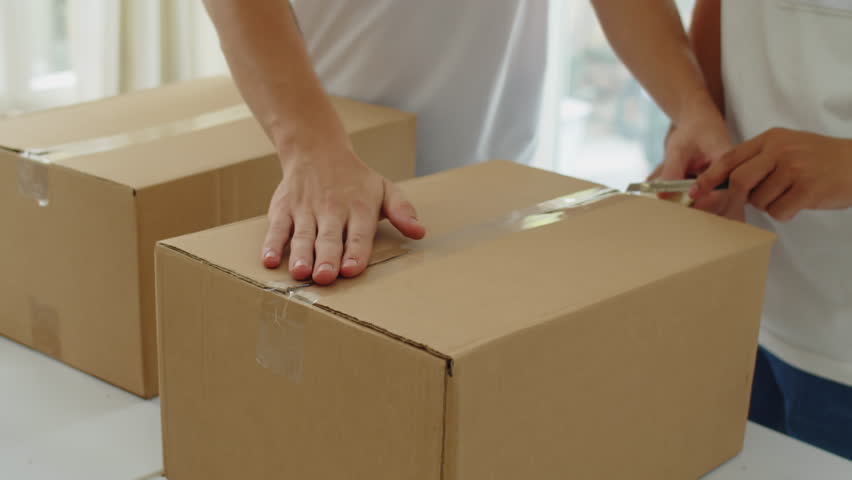 Medium close up of hands of charity organization workers packing donation boxes with tape