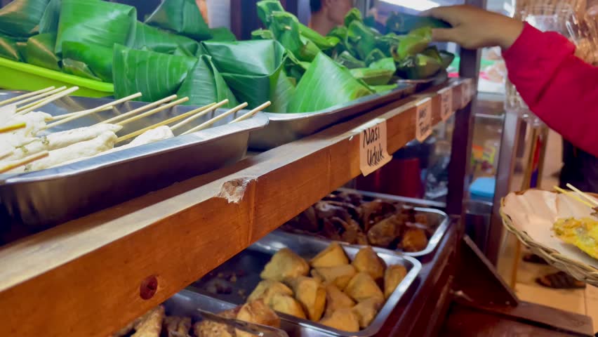 Nasi angkringan or nasi kucing traditional food with egg satay and chicken skin. Hand of men reaching food at display case. it says nasi uduk on the cart which means rice cooked with coconut milk