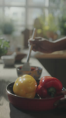 Vertical shot of African American culinary blogger cutting dried tomato on wooden board and telling recipe on camera in kitchen