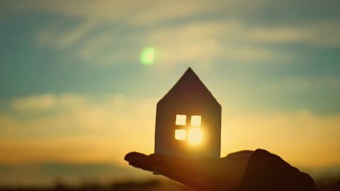 Silhouette hand with paper house at sunset background.