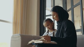 Mother and daughter studying together. Woman wearing hijab and abaya dress teaching and doing homework with her daughter - Powered by Shutterstock - Get 15% off with code: PIKWIZARD15