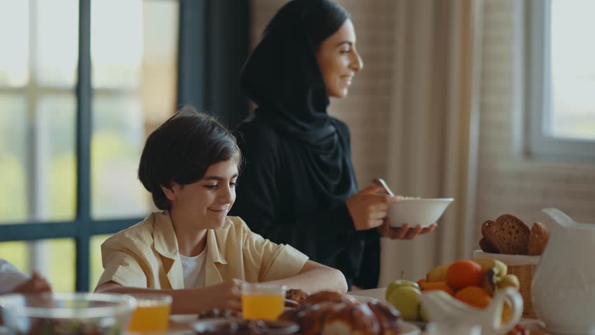 Arabian family from Dubai having lunch together in a cozy apartment. Kids with traditional parents wearing emirati kandura and abaya.
