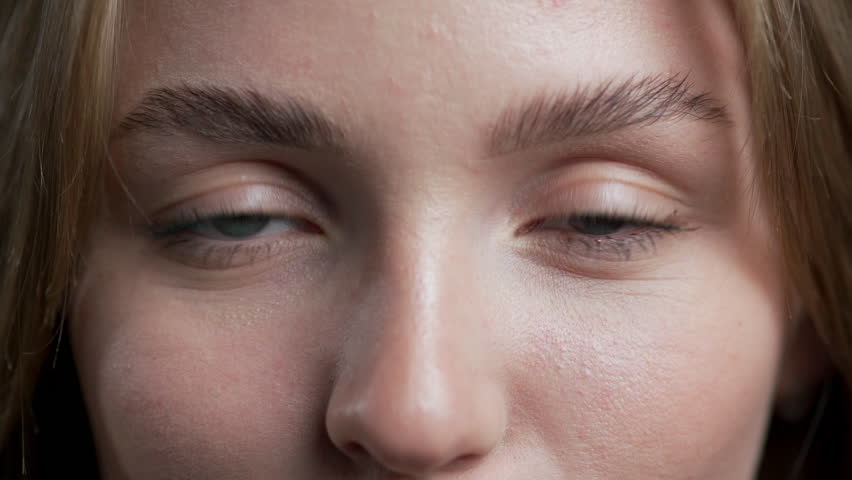 Attractive young woman covering one eye with her hand, looking at the camera.