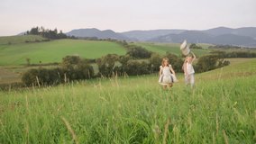Two sisters running with pillows and falling down on the high green grass meadow while they have outdoor natural walking. Family values, traveling 4K footage video concept