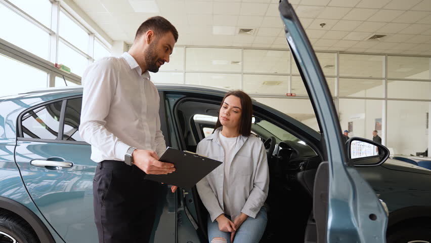 Salesperson in car showroom showing a car to female customer. Right hand drive car