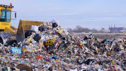 A high pile of trash moved by a landfill truck. Water, air contamination concept.