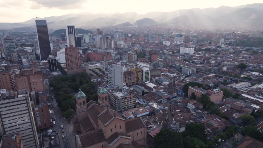 Sun rays pierce clouds lighting urban city of Medellin Colombia and Metropolitan Cathedral of Medellin