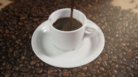Coffee cup and coffee beans. A white cup of evaporating coffee on the table with roasted bean. Slow Motion coffee pour.