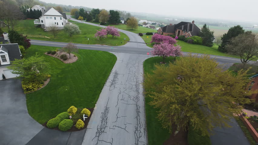 Fpv flight over rural american neighborhood with villas and blooming pink trees. Villa with solar panels on rooftop during foggy day in suburb. Dynamic curvy drone shot.