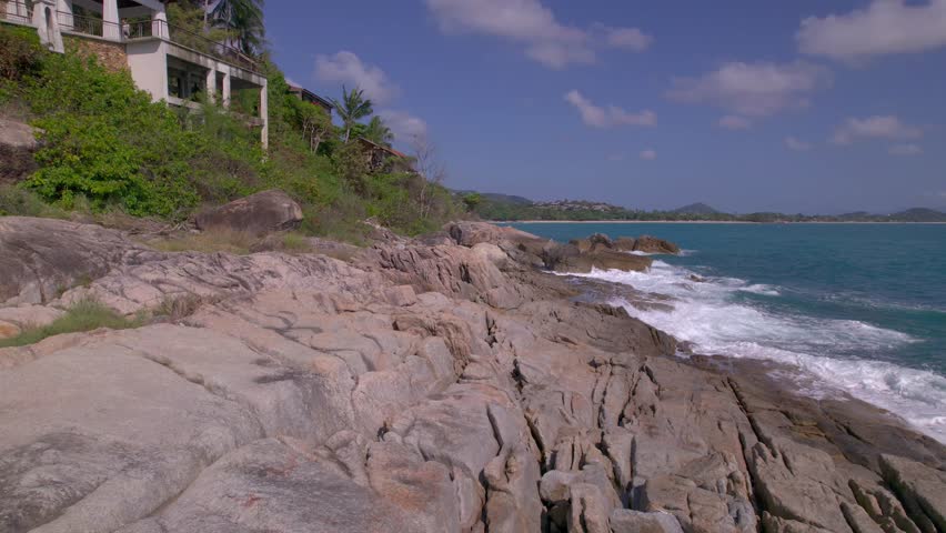 View from above: Coastal terrain with rocky shoreline, house, and azure water