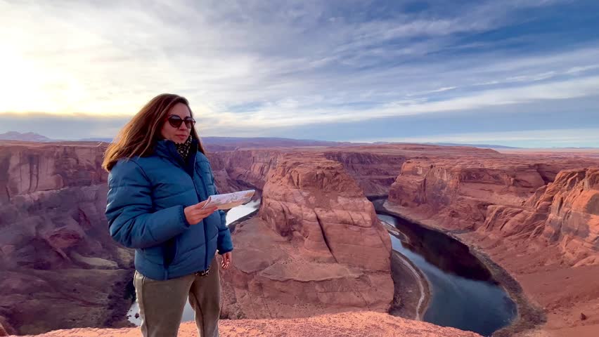 Young female traveler enjoying her solo own vacation time on top of Horseshoe Bend at Glen Grand Canyon National Park in Arizona, United States Of America at sunset time in winter season.