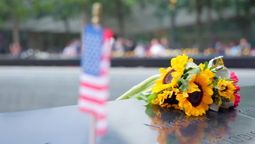 An American flag stands proudly against the backdrop of Ground Zero's reflective memorial, symbolizing resilience and remembrance. September 11 Slow motion.  Royalty-Free Stock Footage #3501515543