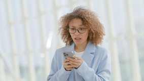 Young businesswoman with curly hair reacts with a surprised expression while reading a text on her smartphone, in a light and airy modern architectural setting. Slow motion.  - Powered by Shutterstock - Get 15% off with code: PIKWIZARD15
