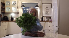 a woman in a blue jumper in a white kitchen making parsley salad