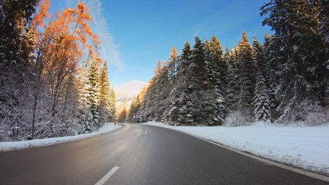 POV vehicle drive across beautiful winter nature, forest evergreen trees with snow, mountains, asphalt road and sunny blue sky, car travel gopro point of view