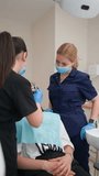 Young Adult Female Dentist with Assistant in Uniform and Medical Masks Does out Teeth Treatment a Patient in a Modern Dental Clinic. Healthcare and Medicine Concept. Slow Motion, Vertical Video