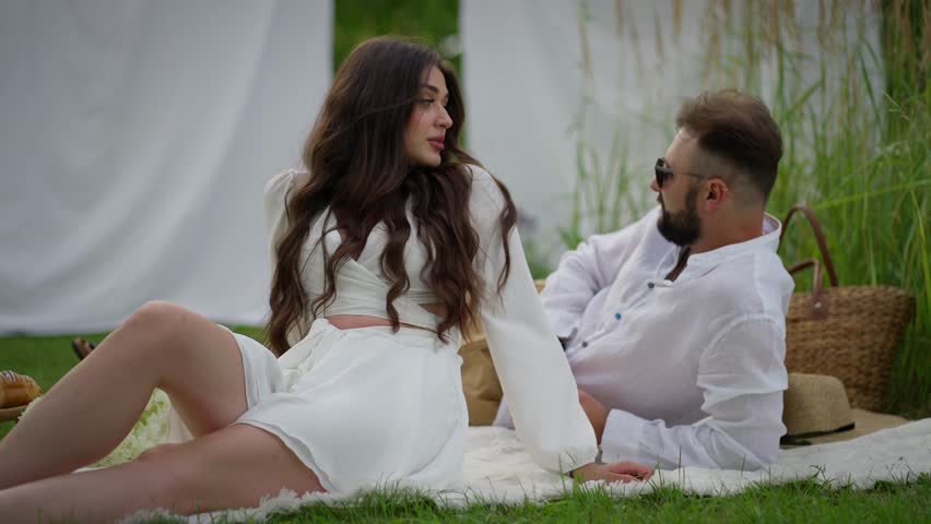 Couple in love on picnic and relaxing in park. Man and woman are relaxing in nature, sitting on picnic with basket. Summer vacation concept
