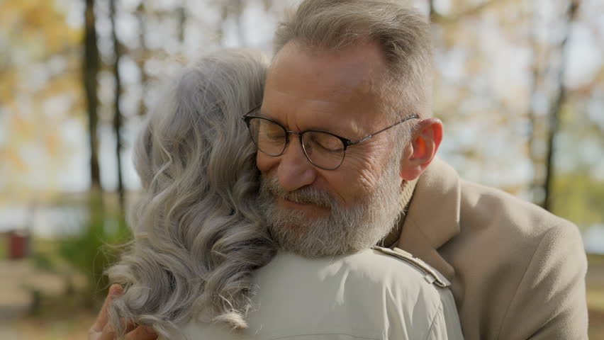 Retired senior mature old Caucasian man embracing cuddling hugging woman affection love couple in park outdoors male female affectionate bonding tender hug embrace husband romantic meet wife in city