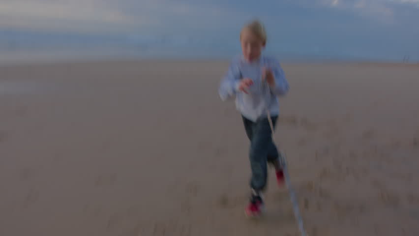 Girl wearing a striped jacket and jeans runs with a small Chihuahua on a sandy beach