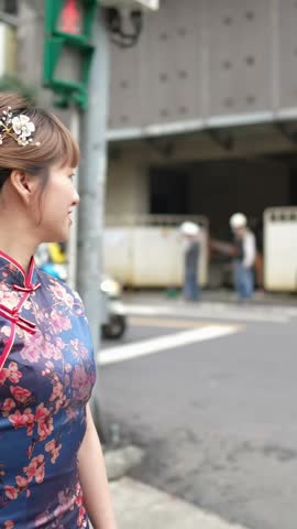 Vertical slow-motion video of a Taiwanese woman in her 20s wearing a blue traditional Chinese dress in Wanhua District, Taipei City, Taiwan, walking on the crosswalk with a smartphone