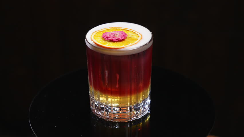Elegant serving of new york sour cocktail with slice of orange wheel and pink dried flower on top for garnish. Bourbon or whiskey with adding of sugar syrup, lemon juice, egg white foam and red wine.