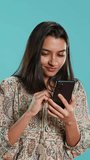Vertical video Woman happily scrolling on phone touchscreen to check social media feed, amazed by photo. Indian person browsing internet websites, astonished by content, studio background, camera A