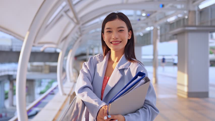 Portrait of Asian youg beautiful businesswoman standing outdoor in city. Attractive employee girl worker feel happy and confident then smile, looking at camera. Job application and recruitment concept