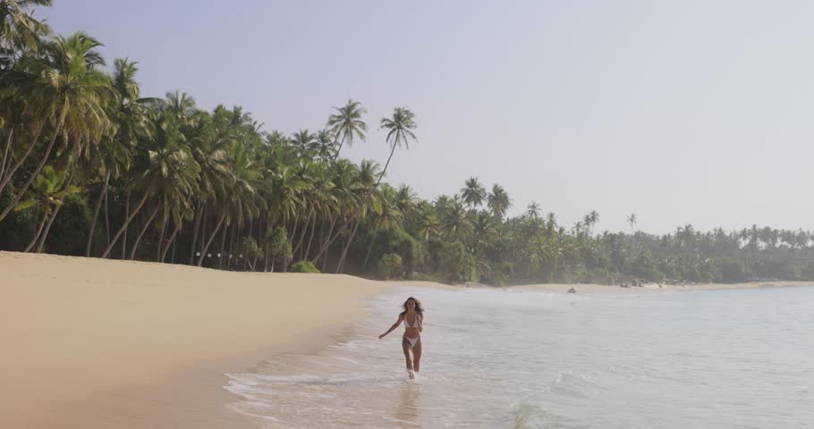 The Bikini girl was overwhelmed by the wave on the beach during vacation. Sexy tanned woman in a white swimsuit with a perfect body smile and have fun at tropical beach. High-quality photo