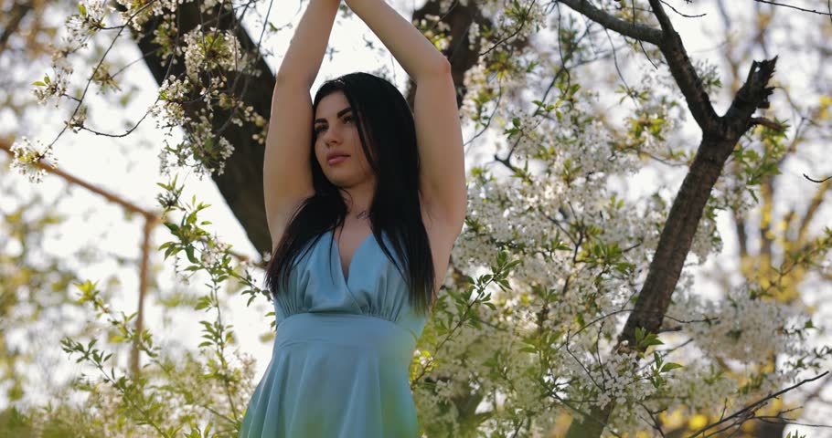 Woman posing in blue dress in a white blossom tree, slow motion