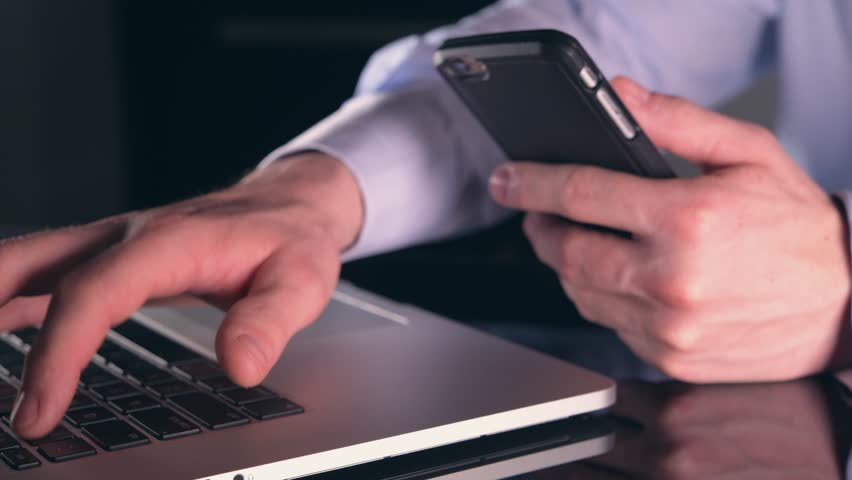 Caucasian Businessman Working Online Using His Laptop Computer and the Smartphone. Mobile Devices Sync.