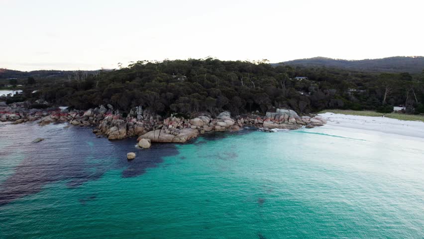 Aerial turquoise blue ocean with fiery red rock coastline and forest