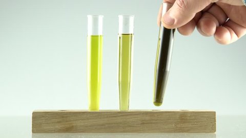 mans hand setting 3 glass tubes with extraction of cannabis oil and ethanol alcohol ,in first is unfiltered oil and ethanol, second is with filtered mix and third is with high concentration of oil