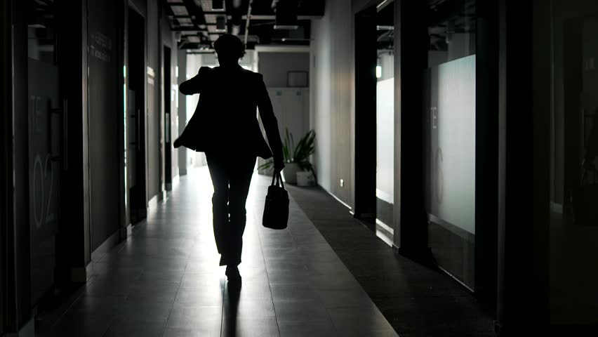 Rear view. The silhouette of a businessman in suit runs along corridor of office building. A confident entrepreneur or manager with a briefcase in his hands is late, rushing to exit of business center