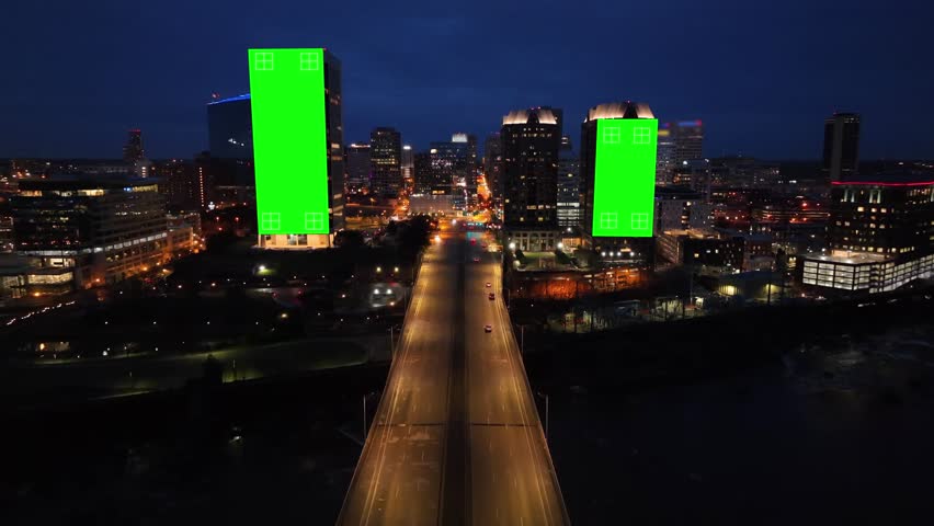 Green screens on skyscrapers in American city at night. Aerial animated drone shot of skyline with billboards with tracking points. Highway, bridge entering downtown.