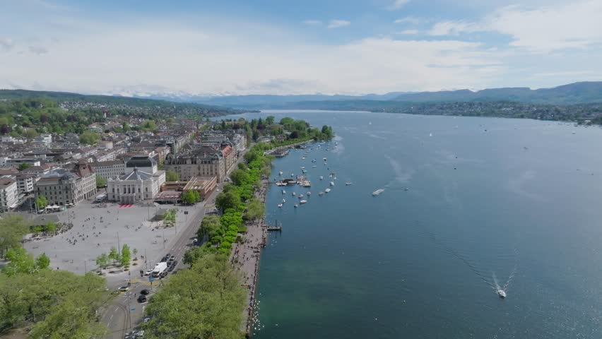 Fast forward moving drone shot showing Zurich opera house, city inhabitants, transport, skyline and the lake front.