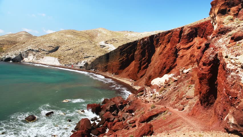 Red beach in Santorini island, Greece. Red volcanic pumice cliffs with black sand on the beach. Blue sea and the blue sky at sunny day. Famous tourist location in Santorini island.

