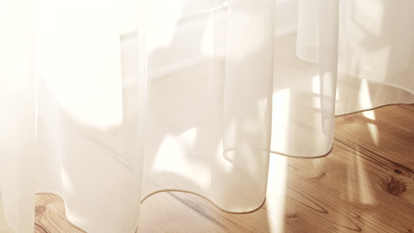 Transparent white curtain tulle moves from the wind from an open window with shadows. Sunny day, the sun's rays sunlight penetrate the room.