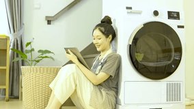 young woman playing video game waiting for washing machine 