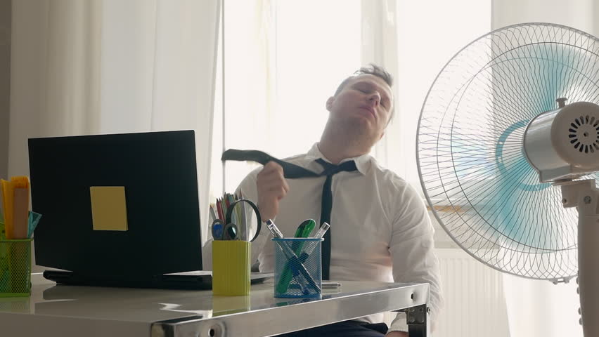 An office worker flutters his tie in the wind. A fan in a worker’s office, a propeller in an office cools a person. Hot Summer