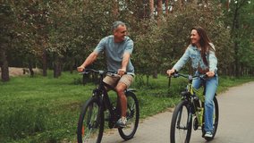 Smiling couple rides bicycles together along park path. Man and woman share joyful moment, cycling side by side surrounded by lush greenery and trees. Outdoor activity promotes healthy lifestyle - Powered by Shutterstock - Get 15% off with code: PIKWIZARD15