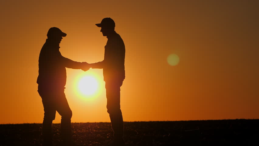 Silhouettes of two farmers shaking hands against the sky where the sun sets