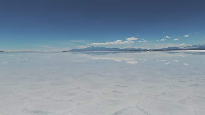 Drone flies over the water surface in the natural salt flat of Salinas Grande. Andean mountains on the horizon. Jujuy, Argentina. 4k.