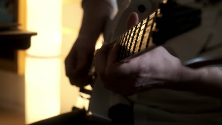 Playing the guitar. Strumming acoustic guitar. Musician plays music. Man fingers holding mediator. Man hand playing guitar neck in dark room. Unrecognizable person rehearsing, fretboard close-up.